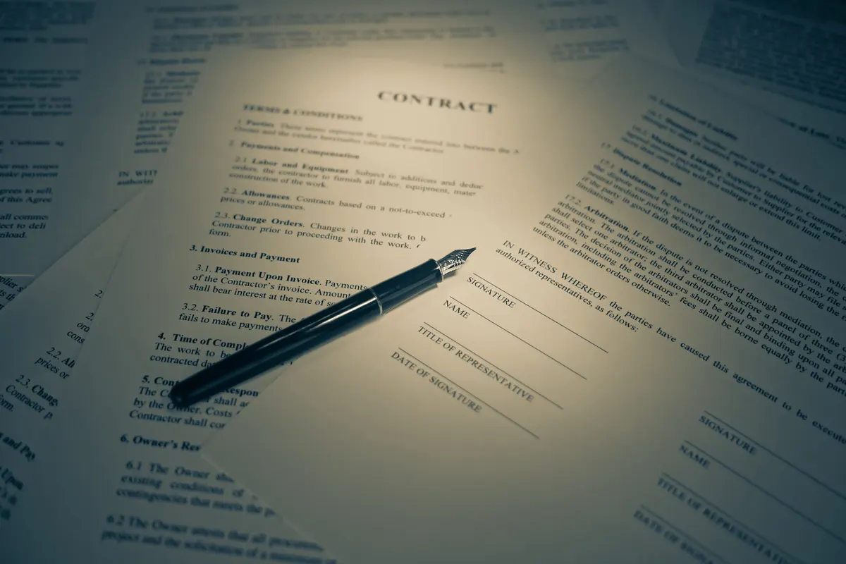 A printed contract with signature lines and a fountain pen resting on top of the pages