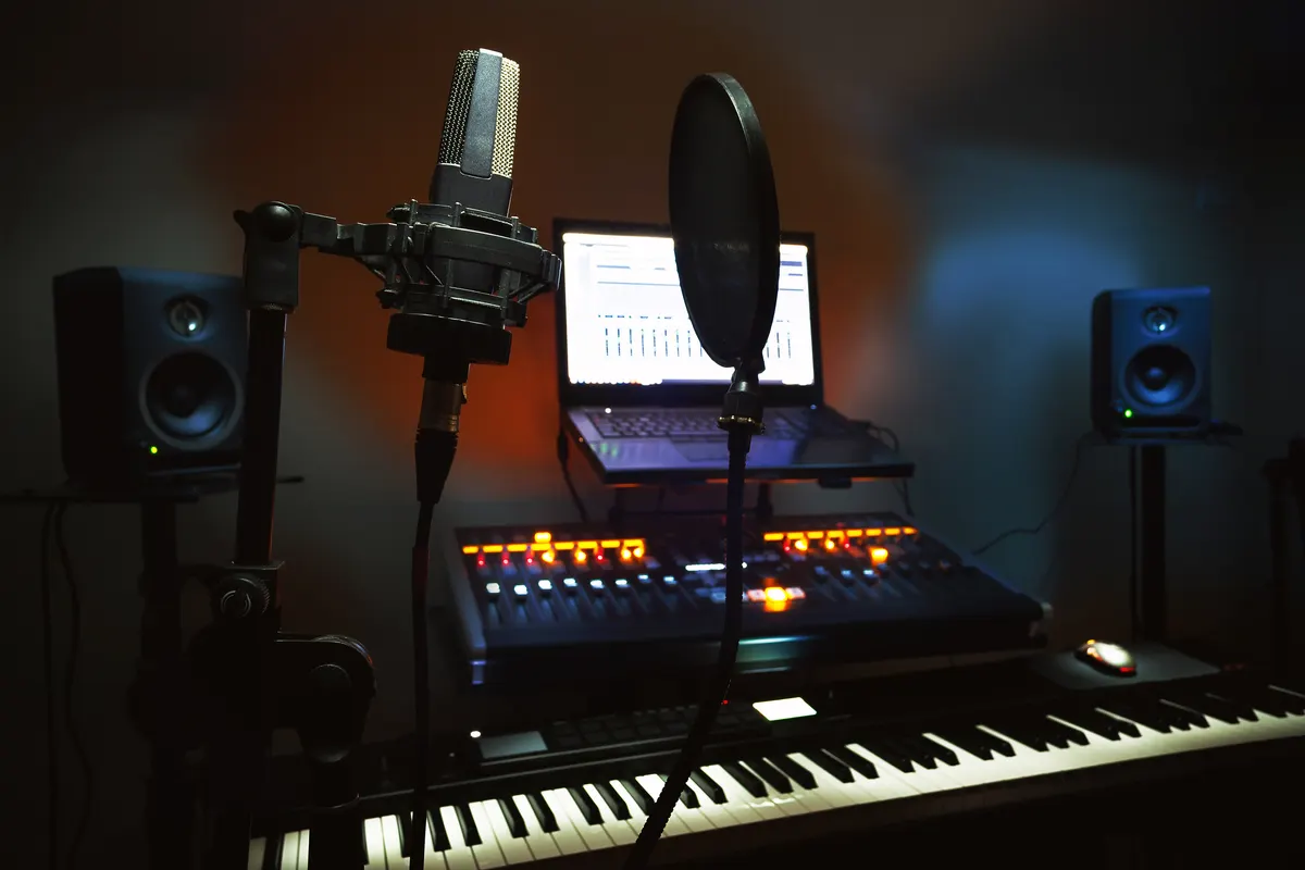 A small home recording studio with a microphone, pop filter, laptop, mixing desk and keyboard