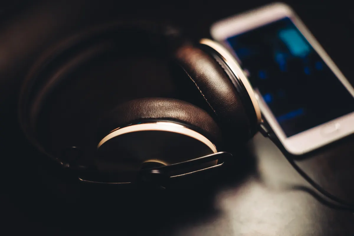 Over-ear headphones lying on a dark table beside a smartphone with a lit screen