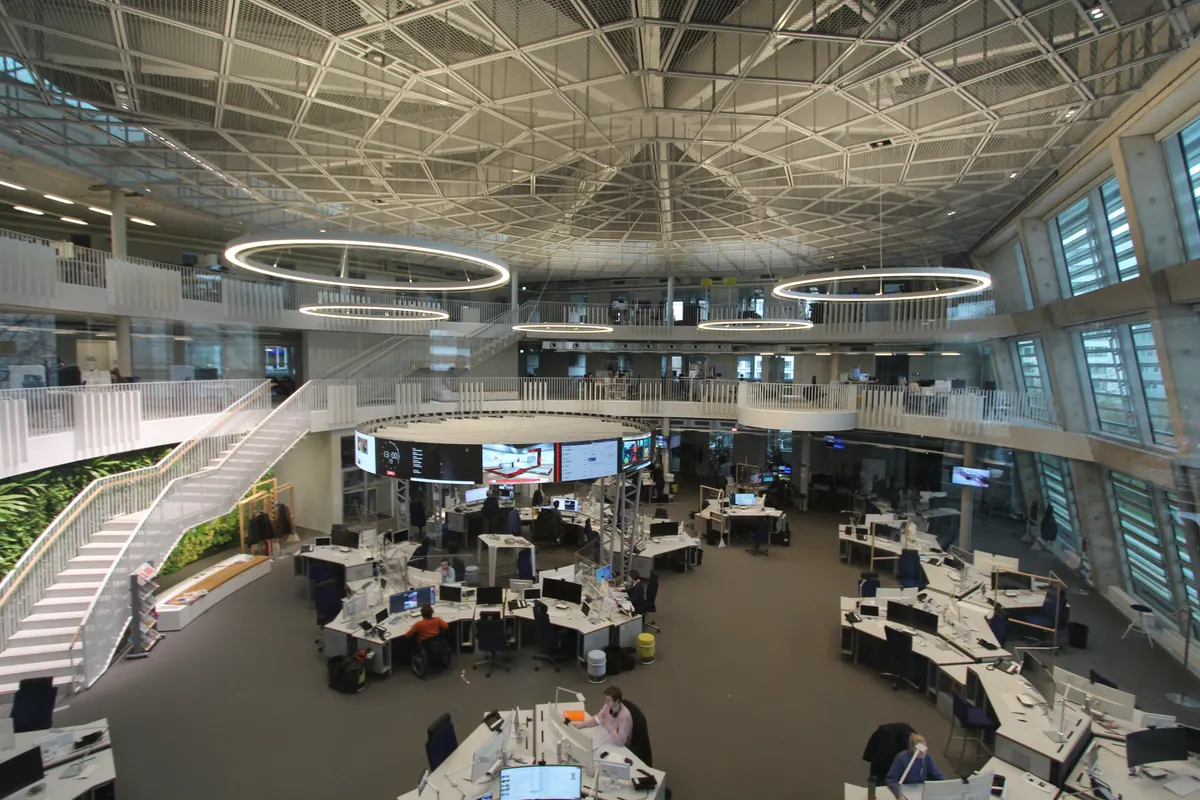 Wide view of a modern newsroom with curved desks, monitors and journalists at work