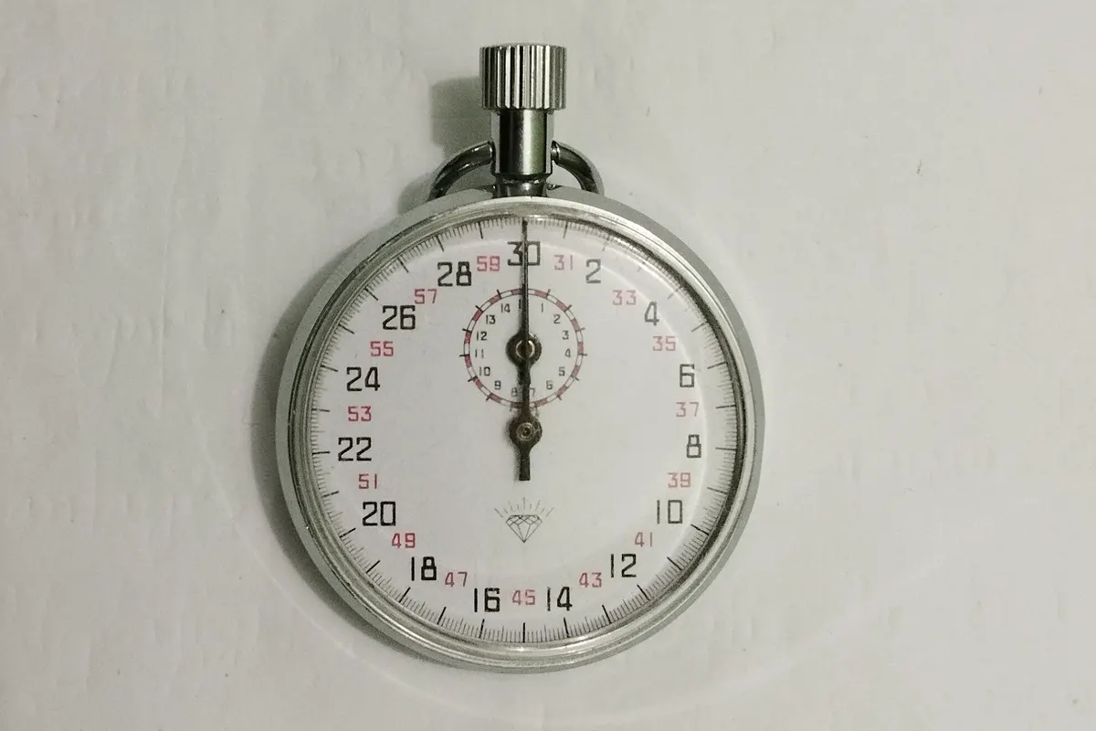An analog stopwatch with a white dial and red and black numbers lying flat