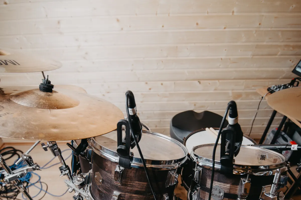 A drum kit with two microphones clipped to the toms in a wood-panelled rehearsal room