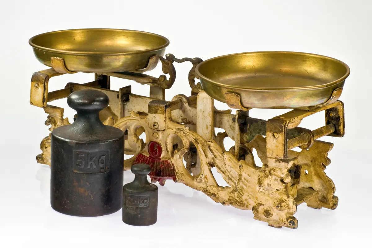 An antique cast-iron balance scale with two brass pans and two black iron weights marked 5 kg