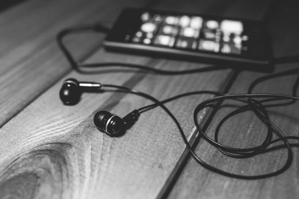 Black earphones and a phone with their cables lying on a wooden table