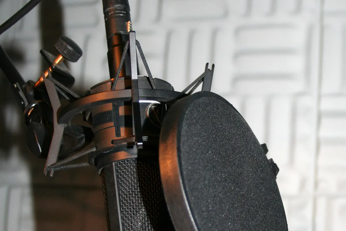 A studio microphone in a shock mount with a round pop filter in front of foam panels