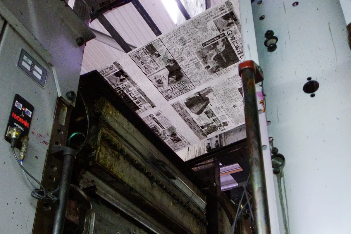 Web-fed offset press printing a newspaper, with printed pages running through the machine