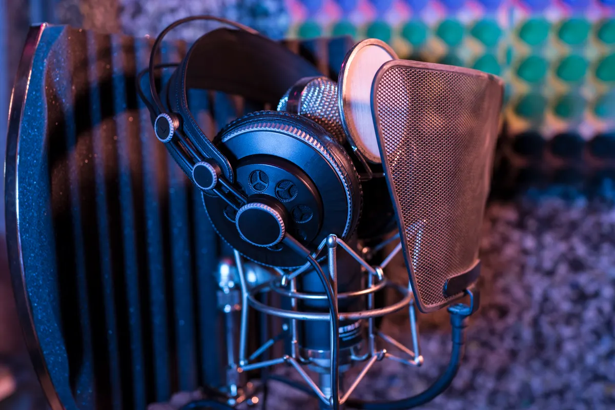 A studio microphone with a pop filter and headphones resting on the stand