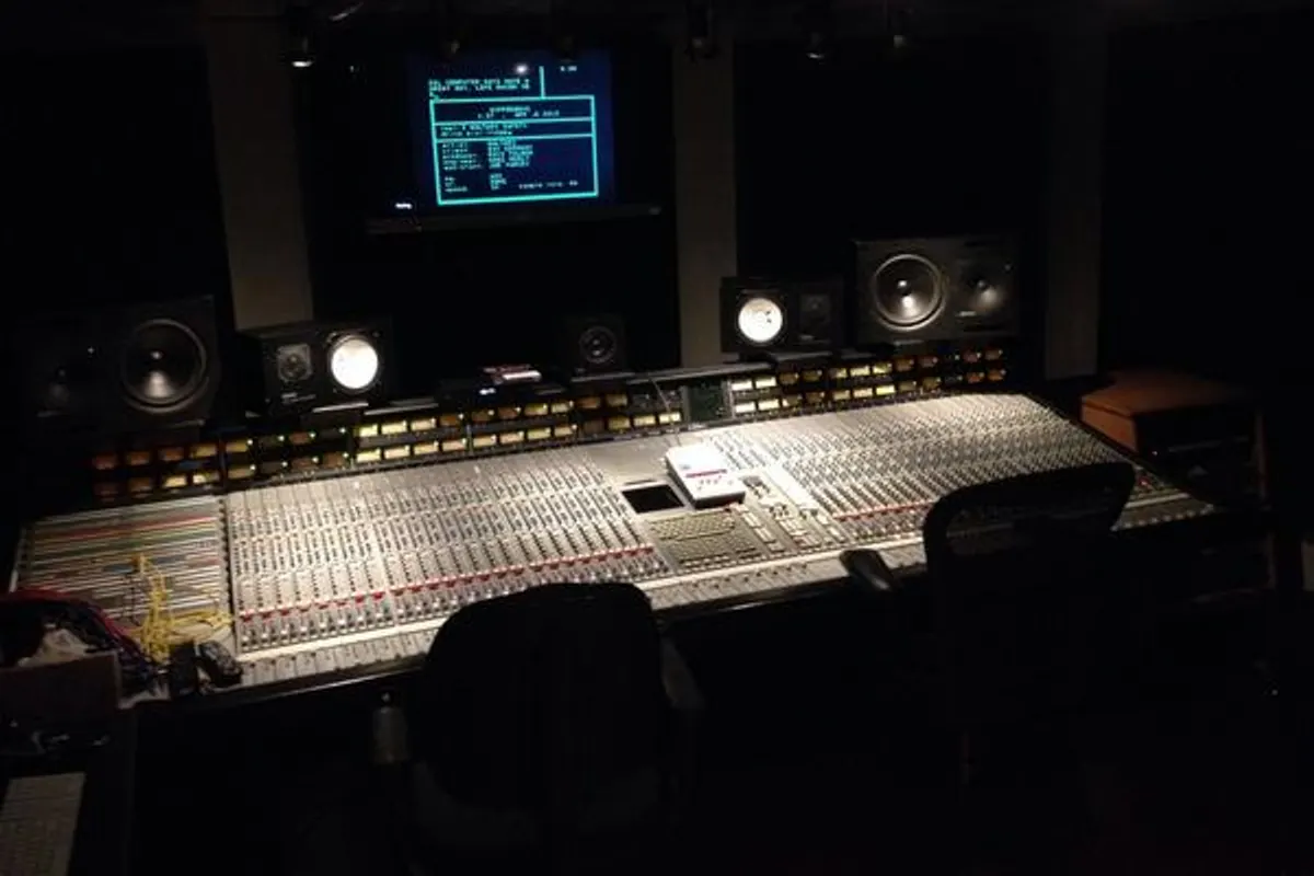 A large analogue mixing desk with rows of faders in a dim recording studio