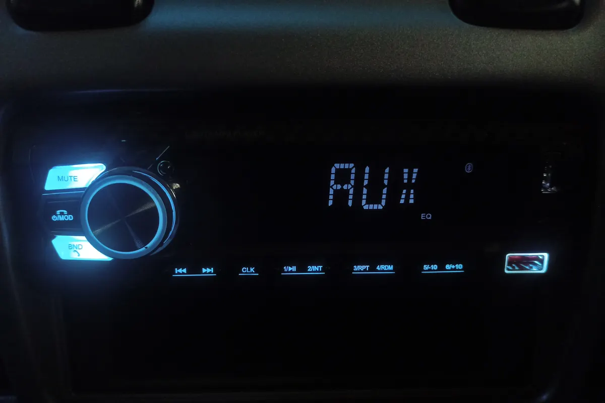 A car stereo head unit glowing blue in a dark dashboard, with a volume knob and buttons